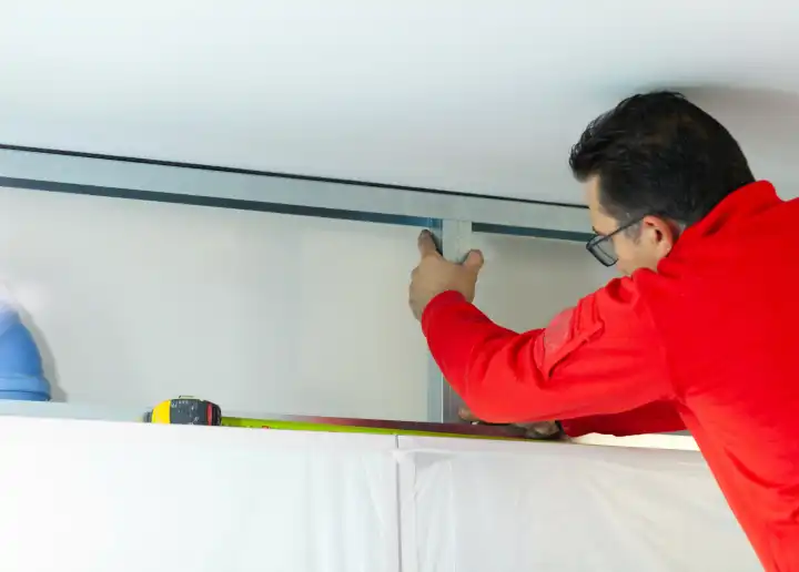 Gipskartonarbeiter installiert eine Gipskartonwand an den Küchenschränken, um das Absaugrohr der Haube abzudecken.