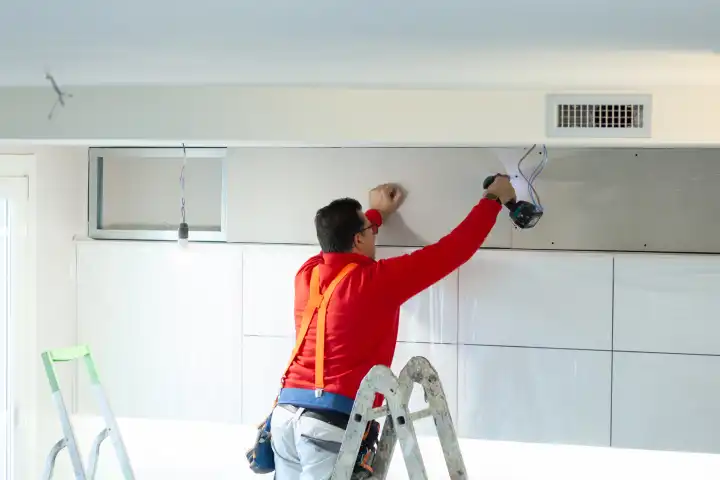 Gipskartonarbeiter installiert eine Gipskartonwand an den Küchenschränken, um das Absaugrohr der Haube abzudecken.