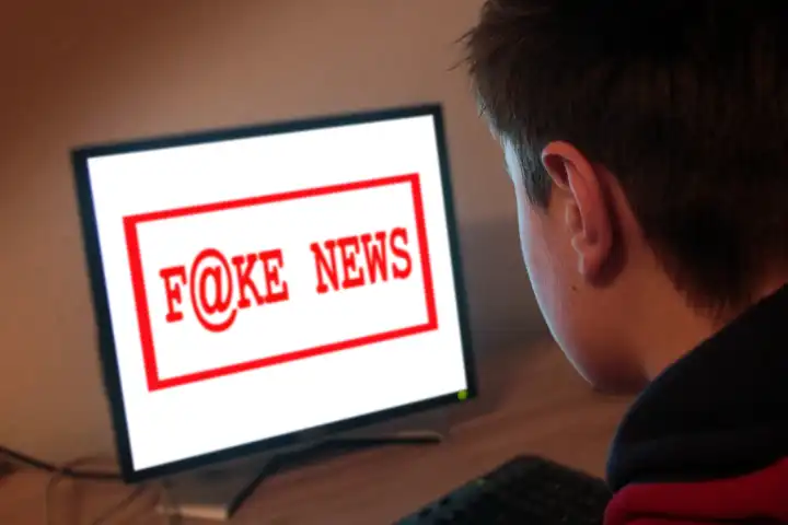 young man in front of a computer with words fake news