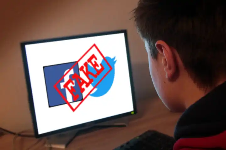 Symbolbild Fake News Jugendlicher sitzt am Computer und schaut auf seinen Bildschirm mit Twitter und Facebook Emblemen