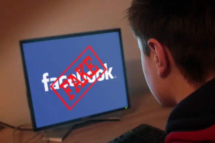 young man in front of a computer with word fake over facebook sign