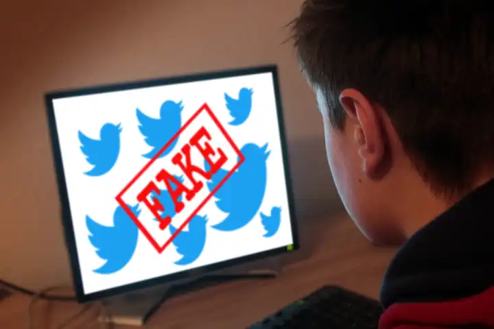 young man in front of a computer with word fake over Twitter signs
