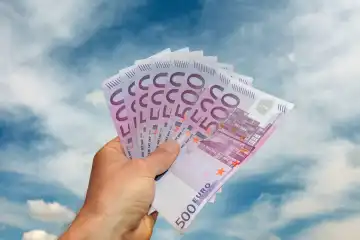 Hand hält einen Fächer mit 500 Euro Banknoten vor blauem Himmel