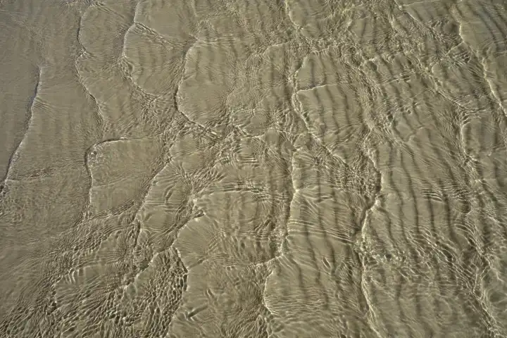 Reflexionen auf Wasser mit gerippeltem Sand im Untergrund