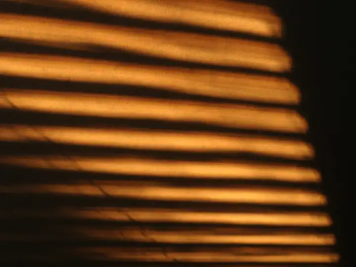 The sun throws its light through the blinds on the wall, reflection