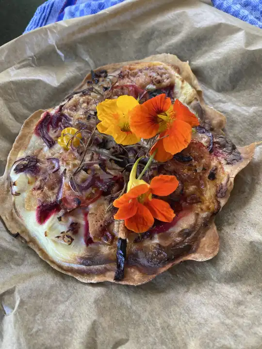 Tarte flambée garnished with edible flowers, nasturtium flowers