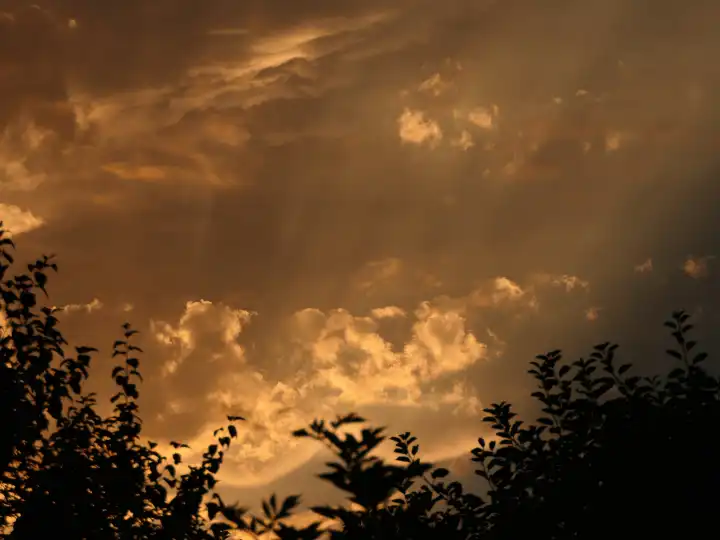 Dramatischer orange-grauer Himmel mit vom restlichen Sonnenlicht des Tages angestrahlten Wolken, Sonne zieht Wasser