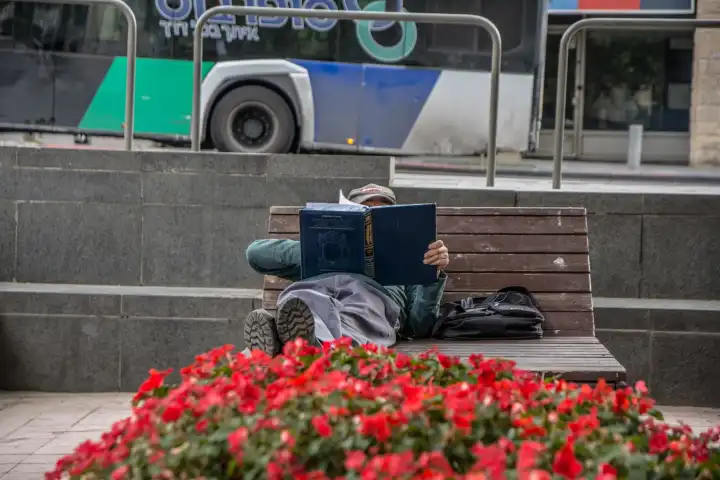 Jemand liest auf einer Bank am Davidka-Platz in Jerusalem im jüdischen Gebetbuch Seder ha-Tefillot.