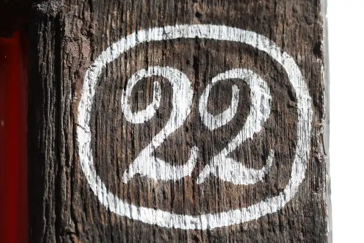 Weisses Hausnummernschild Nummer Zweiundzwanzig auf einen dunklen Holzbalken gemalt, Deutschland