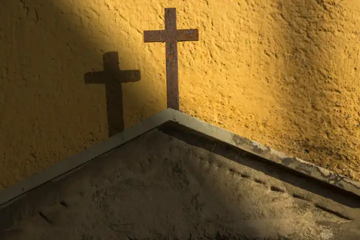 Kreuz auf einem Grabstein an einer gelben Wand im Sonnenstrahl
