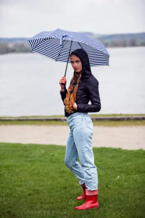Junge Frau mit Regenschirm an einem See auf einer grünen Wiese
