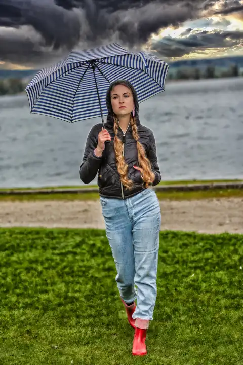 Junge Frau mit Regenschirm an einem See auf einer grünen Wiese