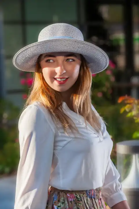 Portrait of a young blonde woman with sun hat and a smile on her lips.