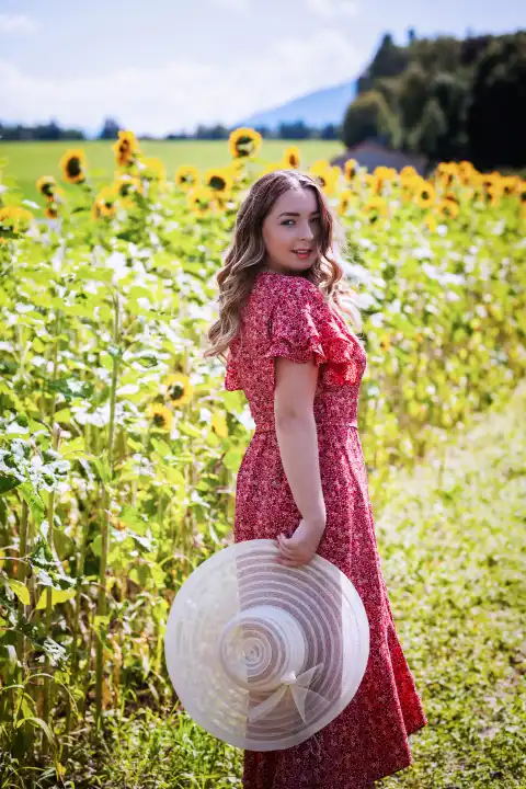 Junge modische Frau mit Hut in der Hand, steht in einem Sonnenblumenfeld