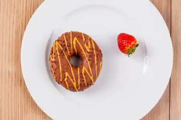 A delicious chocolate doughnut on a white plate, garnished with a fresh strawberry, on a rustic wooden base.