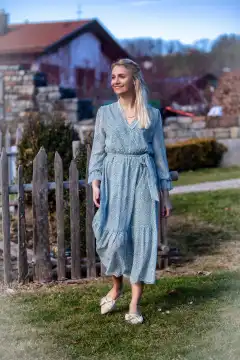 A young woman with blonde hair and a radiant smile strolls through the park on a sunny spring day. She is wearing a fashionable outfit that shows off her figure perfectly. The woman is enjoying the fresh air and the atmosphere of spring.