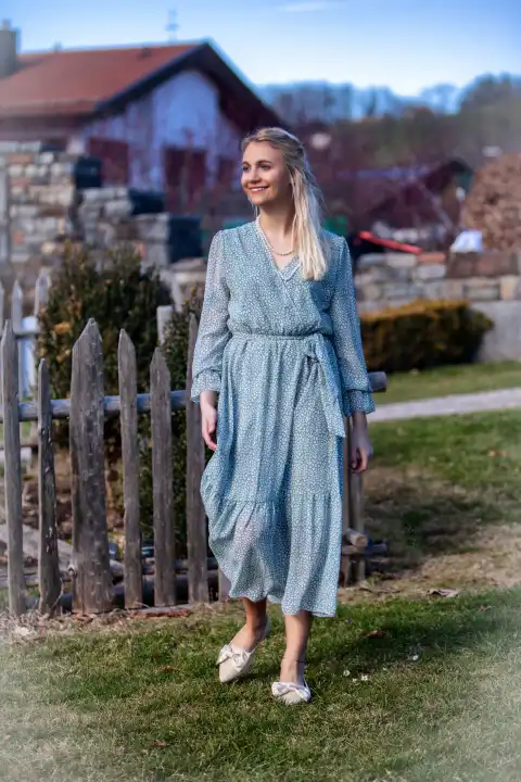 A young woman with blonde hair and a radiant smile strolls through the park on a sunny spring day. She is wearing a fashionable outfit that shows off her figure perfectly. The woman is enjoying the fresh air and the atmosphere of spring.