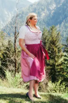 "The picture presents an overweight woman with blonde tresses and a voluptuous décolleté, wearing a traditional Bavarian dirndl. Her friendly smile radiates self-confidence as she presents herself in traditional costume. The dirndl emphasizes her figure, giving her a charming and authentic look."