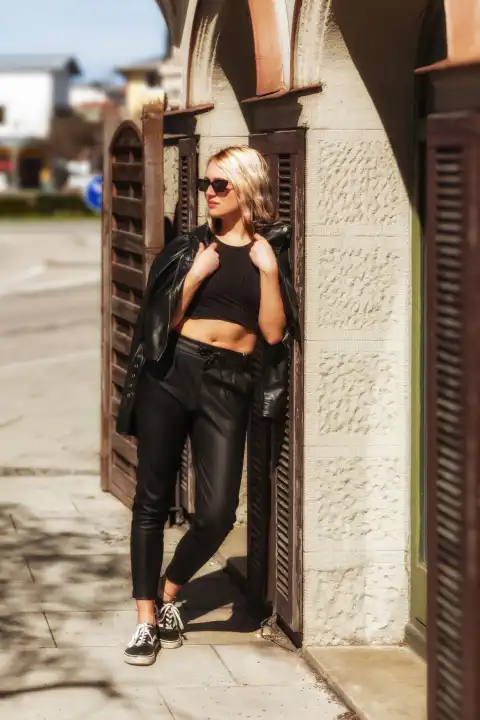 A blonde woman with sunglasses and a summery leather outfit leans casually at the entrance to a café.