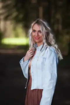 Eine Oberkörperaufnahme zeigt eine junge blonde Frau, die eine offene Jeansjacke trägt, wodurch die Ansätze ihrer Brüste zu sehen sind, was eine verführerische Ästhetik erzeugt.
