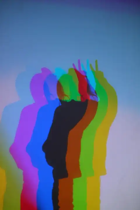 Farbiges Licht wirft Schatten von Person mit V Zeichen