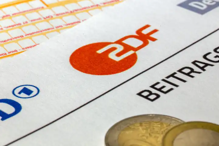 Symbolbild Rundfunkbeitrag, Beitragsservice: Nahaufnahme von einem Briefbogen mit ARD-Logo und ZDF-Logo und einem Überweisungsträger und Geldmünzen
