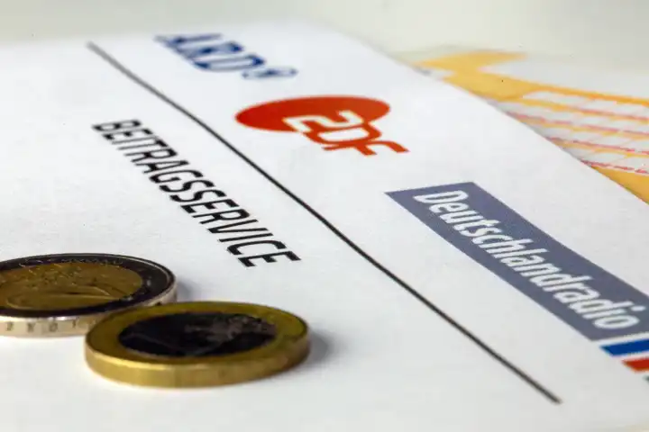 Symbolbild Rundfunkbeitrag, Beitragsservice: Nahaufnahme von einem Briefbogen mit ARD-Logo und ZDF-Logo und einem Überweisungsträger und Geldmünzen