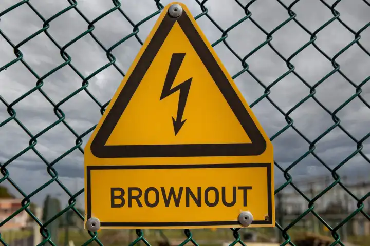 Symbolbild: Unter einem Schild das üblicherweise vor Hochspannung warnt steht das Wort Brownout