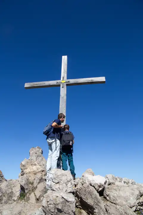 Hiking in the Allgäu Alps: Father and son at the summit cross of the Kanzelwand, 2059 m. above sea level (Model released)