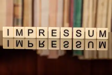 Das Wort im IMPRESSUM mit Buchstabenwürfeln geschrieben vor einem Bücherregal
