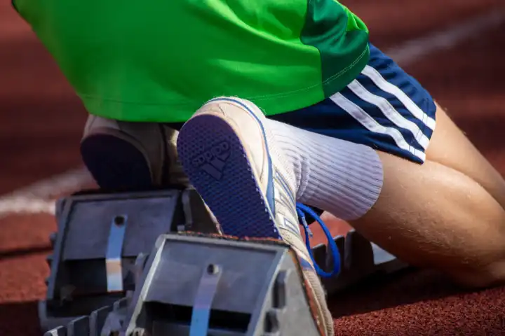 Young track and field athlete with spikes from Adidas at the starting block before a sprint