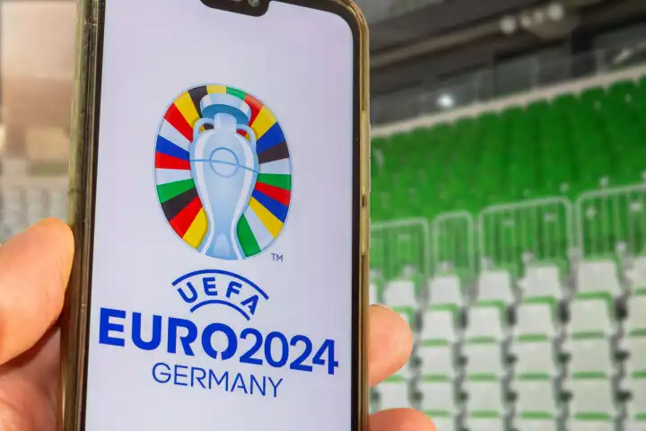 Symbolbild UEFA-EURO 2024: Smartphone mit dem Logo der EURO vor einem leeren Stadion