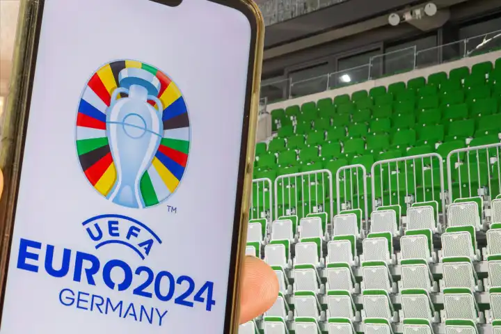 Symbol image UEFA-EURO 2024: Smartphone with the logo of the EURO in front of an empty stadium