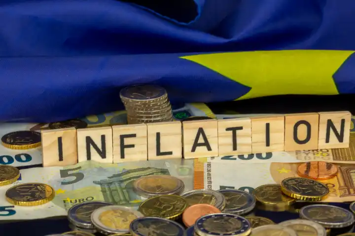 Symbolbild Inflation (im Euro-Raum): Das Wort INFLATION in Buchstabenwürfeln auf Euromünzen und -banknoten 
