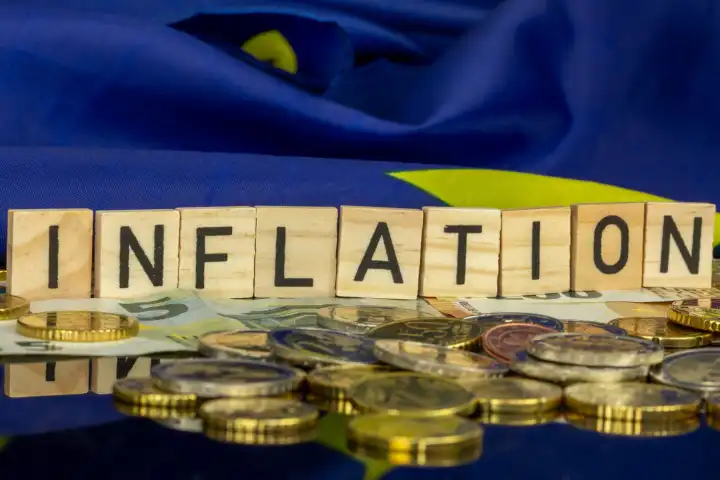 Symbolbild Inflation (im Euro-Raum): Das Wort INFLATION in Buchstabenwürfeln auf Euromünzen und -banknoten 