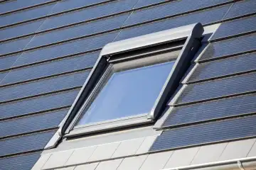 Roof window on a detached house with solar roof tiles. Solar tiles are a beautiful and high-quality alternative to conventional photovoltaic systems