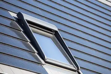 Roof window on a detached house with solar roof tiles. Solar tiles are a beautiful and high-quality alternative to conventional photovoltaic systems