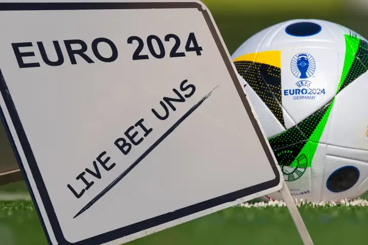 Symbolbild Public Viewing bei der UEFA EURO 2024: Aufsteller mit der Aufschrift EURO 2024 LIVE BEI UNS neben dem offiziellen Spielball (Composing)