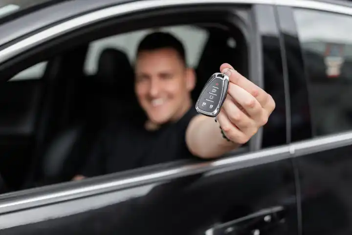 Happy handsome man sitting in car and holding keys. Rent a Car. Purchase of transport