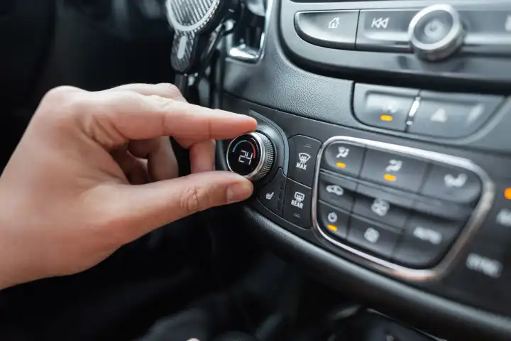 Man's hand turns the climate control wheel in a car. Temperature setting