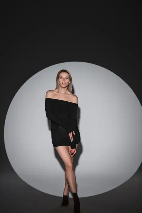 Schöne sinnliche junge Frau in einer schwarzen Mode sexy Kleid steht auf einem dunklen Hintergrund in einem Studio mit kreisförmigen Licht