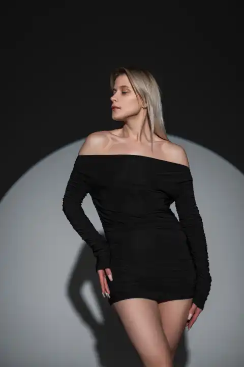 Mode schöne Frau in einem schwarzen sexy Kleid steht auf einem dunklen Hintergrund im Studio