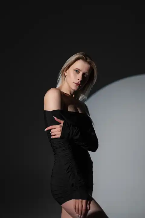 Schöne Mode sinnliche Mädchen in einem schwarzen sexy Kleid steht und posiert im Studio auf einem dunklen Hintergrund