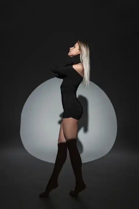 Cool schöne frische natürliche blonde Frau in einem modischen schwarzen sexy Kleid posiert auf einem dunklen Hintergrund mit kreisförmigen Licht