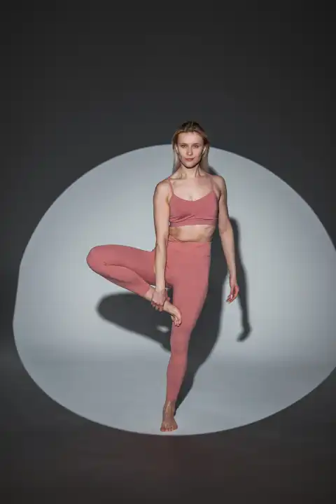 Beautiful fashion sporty slim yoga woman in fashionable sportswear with top and leggings posing and doing exercise in studio on dark background