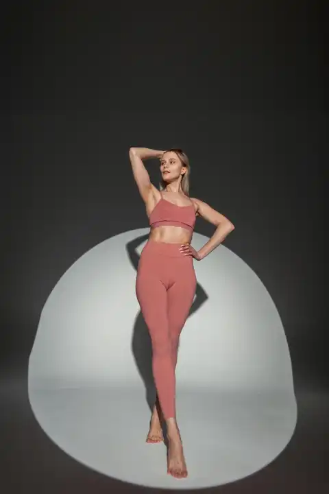 Schlanke schöne sportliche Frau Modell mit einem fitten Körper in Mode Sportbekleidung mit einem Top und Leggings posiert im Studio auf einem dunklen Hintergrund