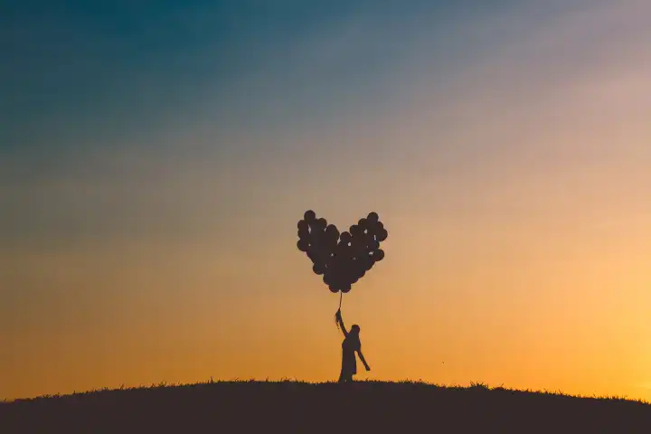 Glückliches Mädchen hält viele herzförmige Luftballons in einem Feld bei Sonnenuntergang. Romantik, Liebe und Freiheit Karte. Träume, kreative Idee