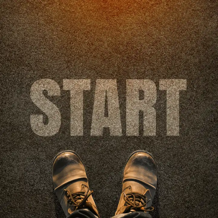 Ein Paar Füße auf einer asphaltierten Straße mit weißem Druck des Wortes Start für das Konzept des Ausgangspunkts. Start Konzept Hintergrund.