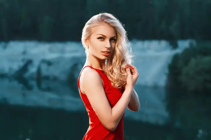 Pretty woman in red dress standing near the mountain. sunset