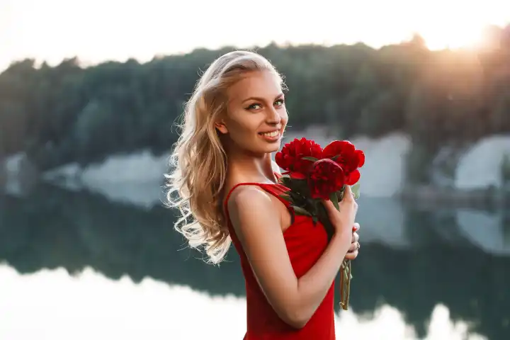 Portrait of a happy pretty woman with a bouquet of peony. On the background of the sea. Sunset light